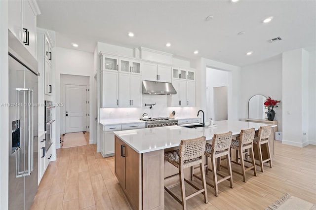 20161 SE Bridgewater Dr, Jupiter, FL 33458 - kitchen featuring under cabinet range hood, light wood-style flooring, a kitchen island with sink, stainless steel built in refrigerator, and recessed lighting