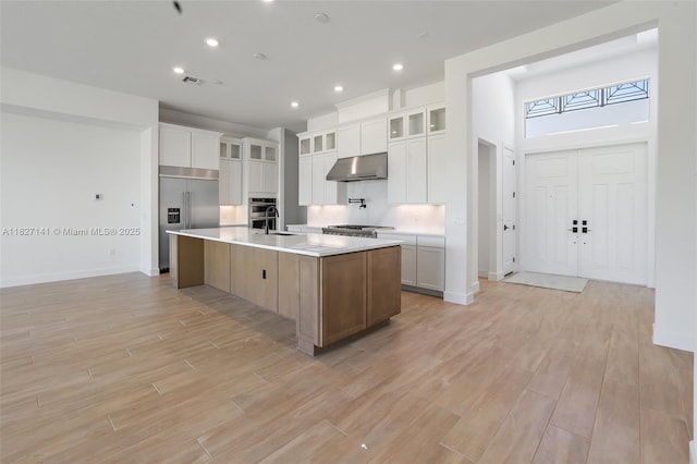 20161 SE Bridgewater Dr, Jupiter, FL 33458 - kitchen with under cabinet range hood, stainless steel appliances, light countertops, light wood-style flooring, and a kitchen island with sink