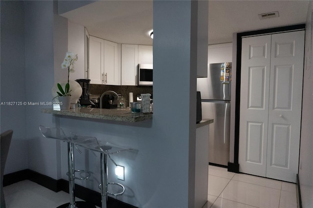8215 SW 152nd Ave Unit G-307, Miami, FL 33193 - kitchen with stainless steel appliances, white cabinets, a breakfast bar area, light tile patterned flooring, and dark stone countertops