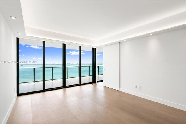 3131 NE 7th Ave Unit 2705, Miami, FL 33137 - empty room featuring a wall of windows, a water view, wood finished floors, recessed lighting, and a raised ceiling