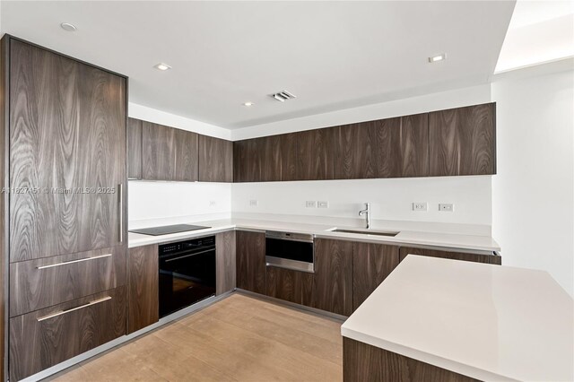 3131 NE 7th Ave Unit 2705, Miami, FL 33137 - kitchen featuring black appliances, modern cabinets, dark brown cabinetry, light countertops, and light wood-type flooring