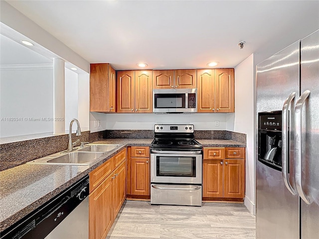 kitchen with appliances with stainless steel finishes, recessed lighting, light wood-style flooring, brown cabinets, and dark stone counters