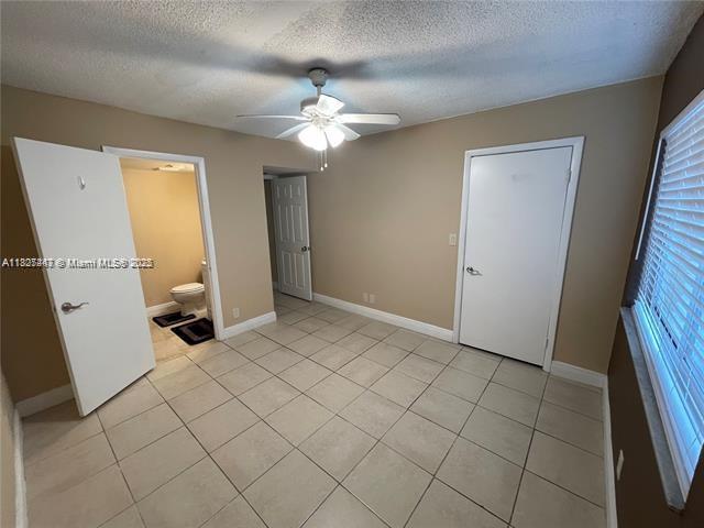 5780 Rock Island Rd Unit 354, Tamarac, FL 33319 - unfurnished bedroom featuring light tile patterned floors, a textured ceiling, a ceiling fan, ensuite bathroom, and multiple windows
