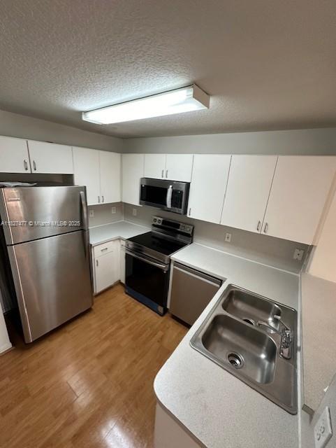11479 NW 60th Ter Unit 372, Doral, FL 33178 - kitchen with appliances with stainless steel finishes, light wood-style flooring, white cabinetry, light countertops, and a textured ceiling