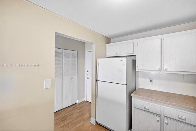 16851 NE 23rd Ave Unit A619, North Miami Beach, FL 33160 - kitchen featuring freestanding refrigerator, light wood finished floors, tile countertops, and white cabinets