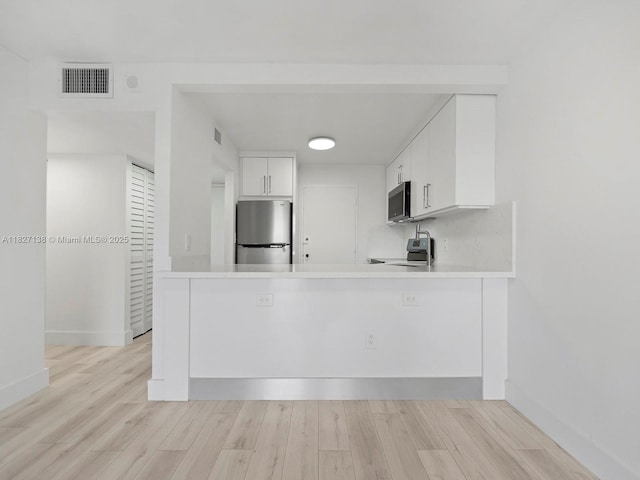 401 Ocean Dr Unit 403, Miami Beach, FL 33139 - kitchen with stainless steel appliances, a peninsula, white cabinetry, light countertops, and light wood finished floors