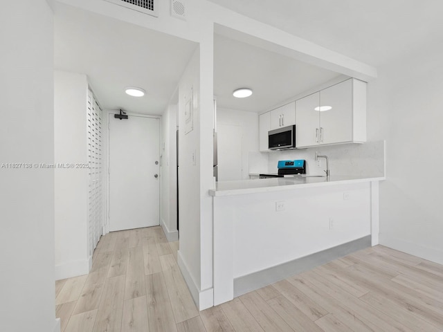 401 Ocean Dr Unit 403, Miami Beach, FL 33139 - kitchen featuring stainless steel microwave, stove, light countertops, white cabinetry, and light wood-style flooring