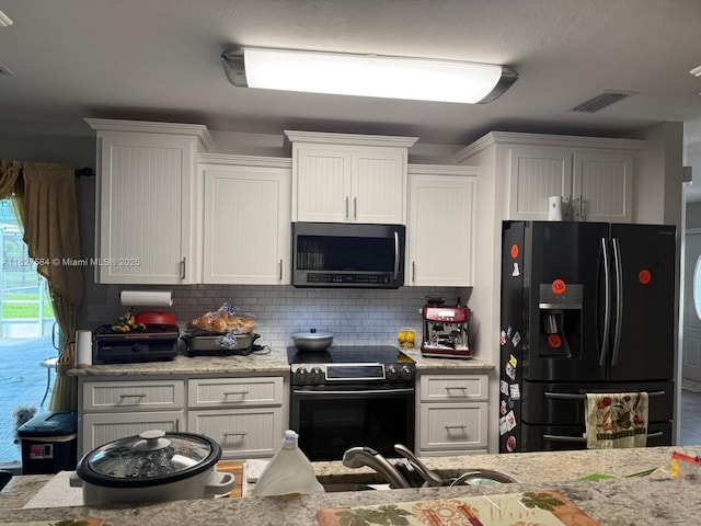 1046 Bayberry Loop, Clewiston, FL 33440 - kitchen featuring black fridge, stainless steel microwave, electric range, decorative backsplash, and white cabinetry