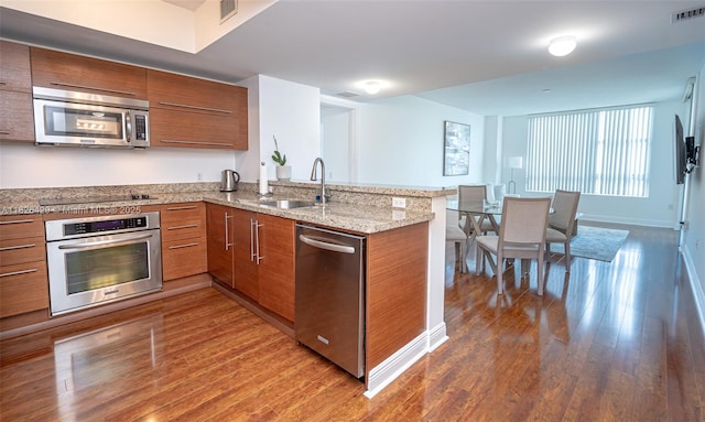 2641 N Flamingo Rd Unit 1603N, Sunrise, FL 33323 - kitchen featuring appliances with stainless steel finishes, brown cabinets, a peninsula, wood finished floors, and light stone countertops