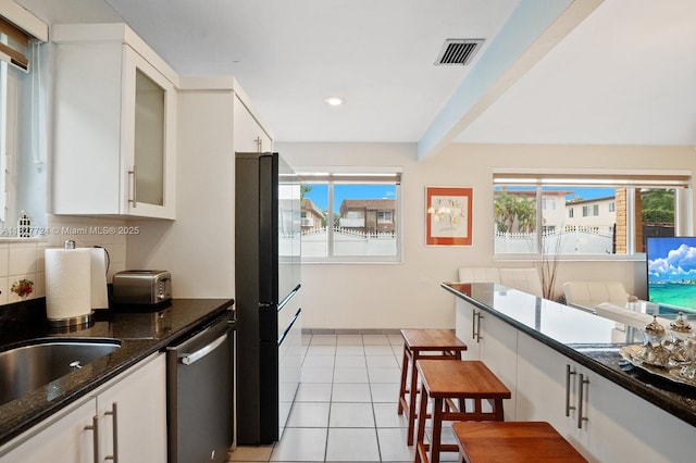 634 82nd St, Miami Beach, FL 33141 - kitchen with stainless steel dishwasher, freestanding refrigerator, white cabinetry, light tile patterned flooring, and dark stone countertops
