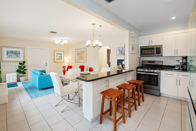 634 82nd St, Miami Beach, FL 33141 - kitchen with appliances with stainless steel finishes, a kitchen breakfast bar, light tile patterned floors, dark countertops, and a chandelier
