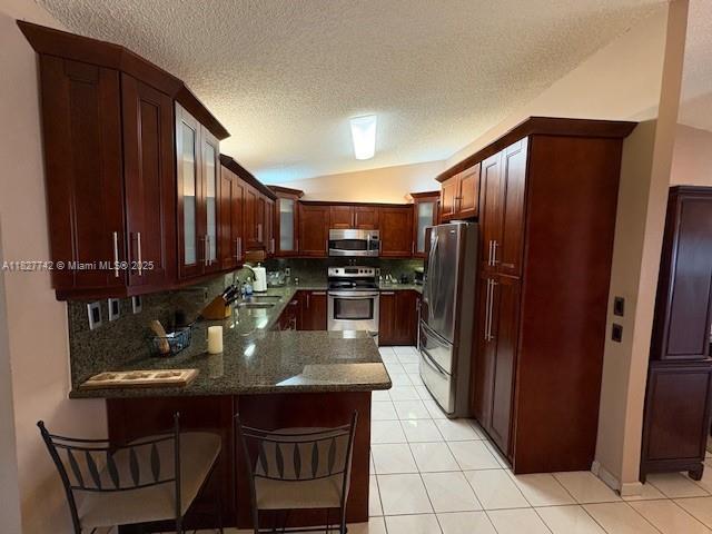 13736 SW 12th St, Miami, FL 33184 - kitchen featuring appliances with stainless steel finishes, a peninsula, a textured ceiling, vaulted ceiling, and glass insert cabinets