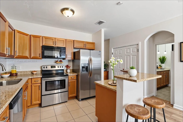 2872 SW 127th Way Unit 1, Miramar, FL 33027 - kitchen with appliances with stainless steel finishes, a breakfast bar, arched walkways, light stone counters, and brown cabinetry