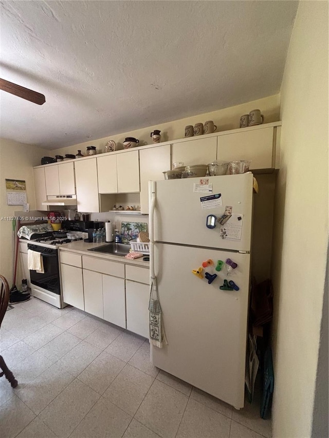 981 E 18th St, Hialeah, FL 33013 - kitchen with freestanding refrigerator, gas range, under cabinet range hood, white cabinetry, and a ceiling fan