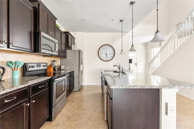 1892 Gobi Dr, Kissimmee, FL 3474 - kitchen with appliances with stainless steel finishes, a kitchen island with sink, tasteful backsplash, light stone counters, and a textured ceiling