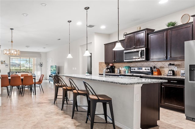 1892 Gobi Dr, Kissimmee, FL 3474 - kitchen featuring stainless steel appliances, backsplash, a breakfast bar area, light stone counters, and a chandelier