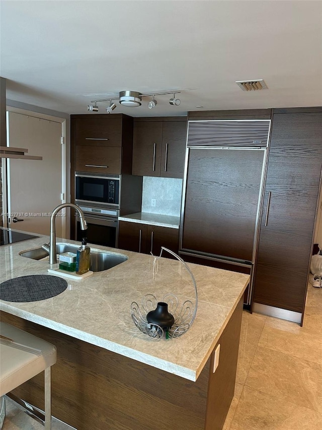 495 Brickell Ave Unit 5211, Miami, FL 33131 - kitchen with built in appliances, modern cabinets, dark brown cabinetry, light tile patterned flooring, and light stone countertops