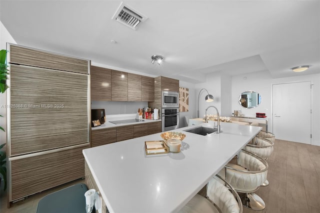 460 NE 28th St Unit 2407, Miami, FL 33137 - kitchen featuring stainless steel appliances, a breakfast bar, brown cabinetry, light countertops, and an island with sink