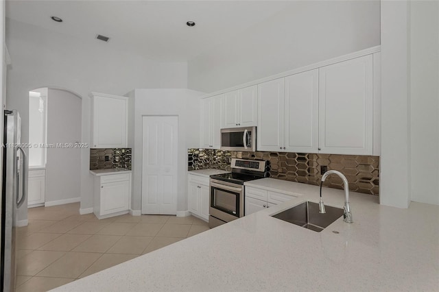 3843 Oak Ridge Cir, Weston, FL 33331 - kitchen featuring appliances with stainless steel finishes, tasteful backsplash, white cabinets, a towering ceiling, and arched walkways