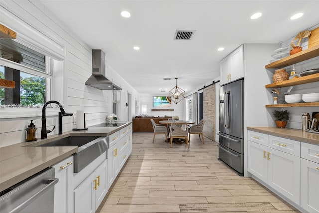 228 Rutland Blvd, West Palm Beach, FL 33405 - kitchen featuring stainless steel appliances, wall chimney exhaust hood, a barn door, open shelves, and light wood-type flooring