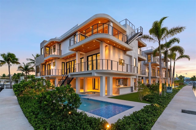 301 Buttonwood Cir # B, Key Largo, FL 33037 - back of house at dusk featuring a balcony, stucco siding, a pool with connected hot tub, a patio, and stairs
