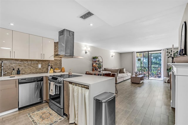 20367 W Country Club Dr Unit L25, Aventura, FL 33180 - kitchen with stainless steel appliances, wall chimney range hood, a peninsula, light wood-style floors, and decorative backsplash
