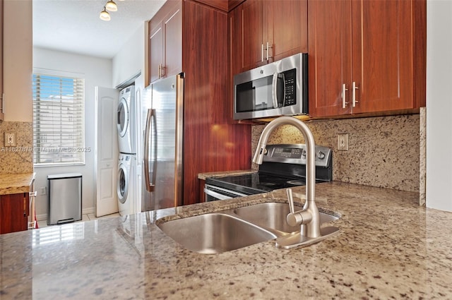8366 NW 10th St Unit 3B, Miami, FL 33126 - kitchen featuring appliances with stainless steel finishes, stacked washing machine and dryer, decorative backsplash, light stone countertops, and brown cabinetry