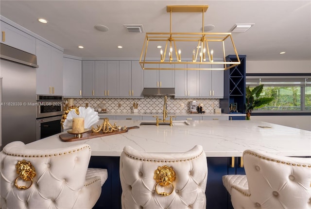475 Bahia Honda Rd, Key Largo, FL 33037 - kitchen featuring stainless steel double oven, under cabinet range hood, backsplash, light stone countertops, and a kitchen breakfast bar