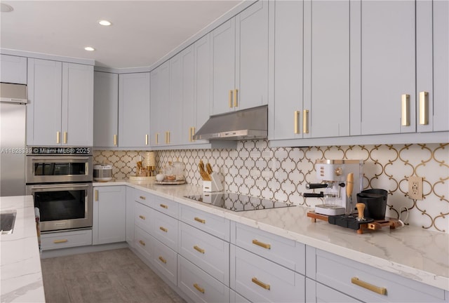 475 Bahia Honda Rd, Key Largo, FL 33037 - kitchen with under cabinet range hood, black electric cooktop, stainless steel double oven, light stone countertops, and recessed lighting