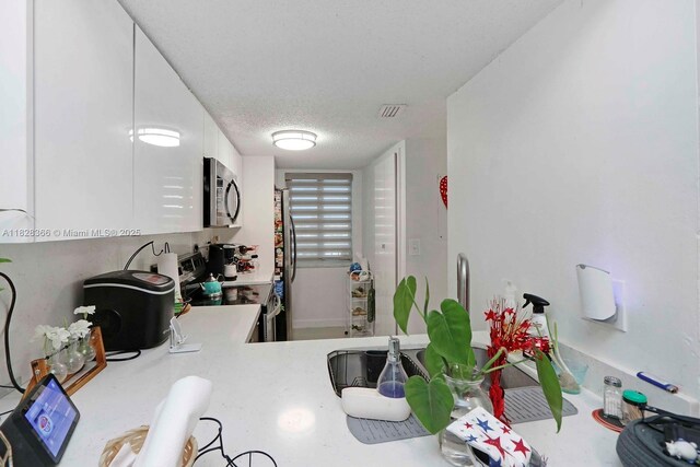 9917 W Okeechobee Rd Unit 3-303, Hialeah Gardens, FL 33016 - kitchen with stainless steel appliances, light countertops, white cabinets, and a textured ceiling