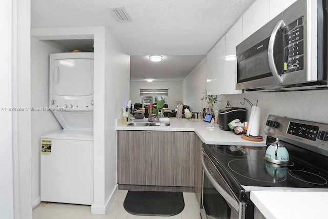 9917 W Okeechobee Rd Unit 3-303, Hialeah Gardens, FL 33016 - kitchen with stainless steel appliances, stacked washer / drying machine, modern cabinets, light countertops, and light tile patterned floors
