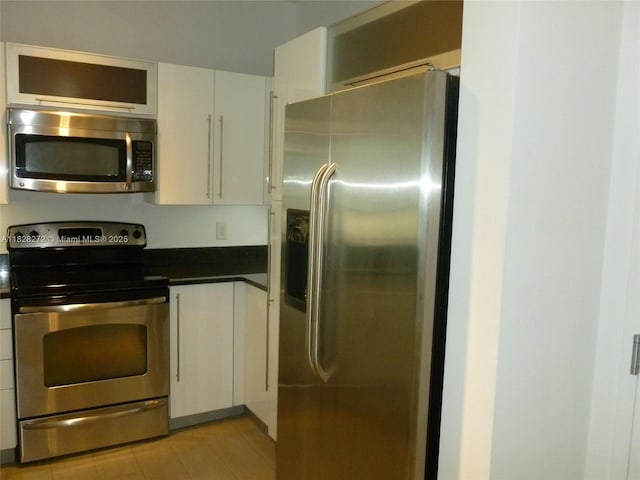 7350 SW 89th St Unit 808S, Miami, FL 33156 - kitchen featuring stainless steel appliances, dark countertops, white cabinets, light tile patterned flooring, and glass insert cabinets