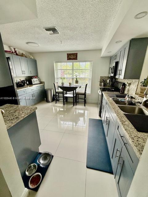 767 SE 22nd Dr, Homestead, FL 33033 - kitchen featuring stainless steel appliances, a textured ceiling, light tile patterned floors, tasteful backsplash, and light stone counters