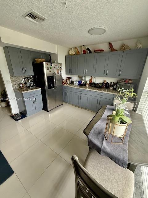 767 SE 22nd Dr, Homestead, FL 33033 - kitchen featuring stainless steel fridge with ice dispenser, gray cabinetry, a textured ceiling, light tile patterned flooring, and decorative backsplash
