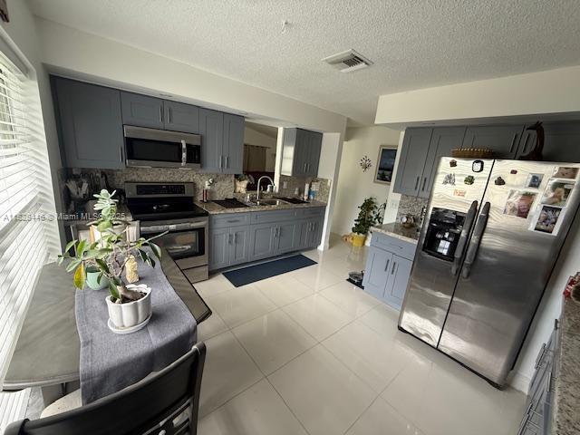 767 SE 22nd Dr, Homestead, FL 33033 - kitchen featuring stainless steel appliances, gray cabinets, tasteful backsplash, and a textured ceiling