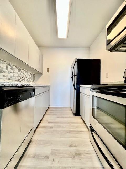 2020 NE 135th St Unit 407, North Miami, FL 33181 - kitchen featuring appliances with stainless steel finishes, tasteful backsplash, light wood-type flooring, and white cabinets