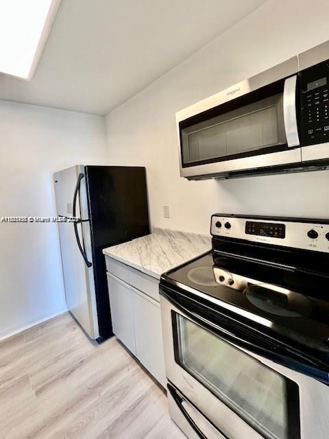 2020 NE 135th St Unit 407, North Miami, FL 33181 - kitchen with stainless steel appliances, light wood-style flooring, and light stone countertops