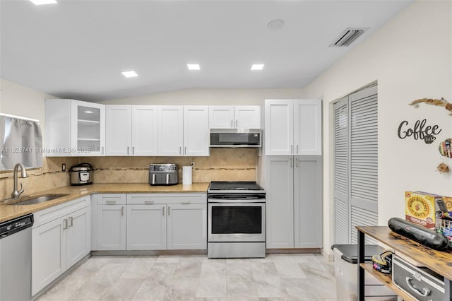 6601 Branch St, Hollywood, FL 33024 - kitchen featuring appliances with stainless steel finishes, backsplash, glass insert cabinets, white cabinetry, and vaulted ceiling