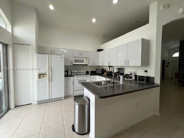 1988 SE 12th St, Homestead, FL 33035 - kitchen with white appliances, vaulted ceiling, a peninsula, light tile patterned floors, and white cabinets
