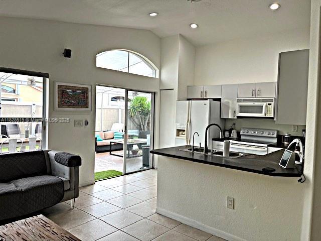 1988 SE 12th St, Homestead, FL 33035 - kitchen featuring vaulted ceiling, dark countertops, white fridge with ice dispenser, light tile patterned floors, and stove