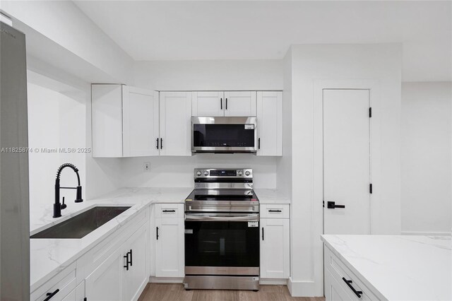 4290 NW 38th Ave, Lauderdale Lakes, FL 33309 - kitchen with stainless steel appliances, white cabinetry, light stone counters, and light wood-style flooring