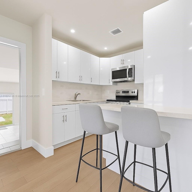 3455 E 1st Ct, Hialeah, FL 33013 - kitchen with stainless steel appliances, a kitchen bar, light countertops, light wood finished floors, and white cabinetry