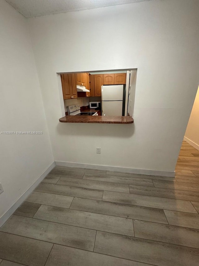 8075 NW 7th St Unit 318, Miami, FL 33126 - kitchen with white appliances, under cabinet range hood, wood finished floors, dark countertops, and brown cabinets