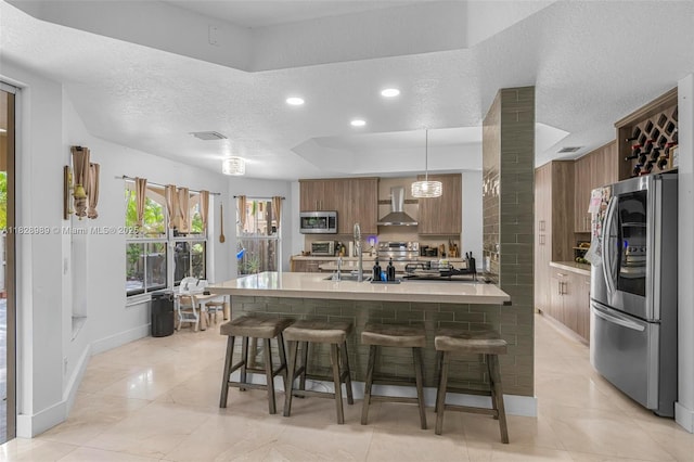 2620 SW 150th Ct, Miami, FL 33185 - kitchen featuring stainless steel appliances, wall chimney range hood, a breakfast bar area, light countertops, and a textured ceiling
