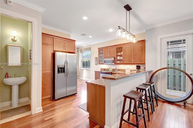 1110 SE 4th Ave, Fort Lauderdale, FL 33316 - kitchen with appliances with stainless steel finishes, a kitchen bar, crown molding, brown cabinets, and a peninsula