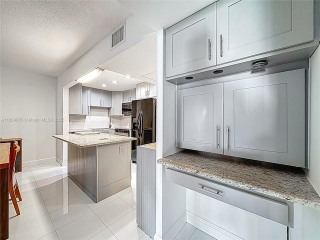 101 E Mcnab Rd Unit 311, Pompano Beach, FL 33060 - kitchen featuring light tile patterned flooring, light stone counters, black fridge, a center island, and a textured ceiling