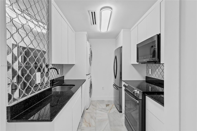 10275 Collins Ave Unit 1035, Bal Harbour, FL 33154 - kitchen with black appliances, stacked washer and clothes dryer, white cabinets, tasteful backsplash, and dark stone countertops