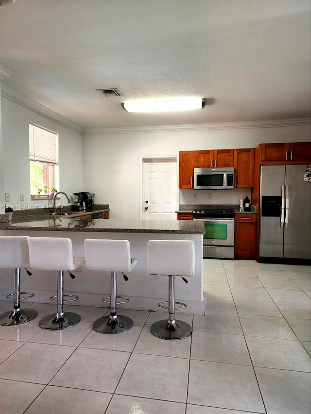 10878 NW 51st Ln, Doral, FL 33178 - kitchen featuring stainless steel appliances, ornamental molding, a breakfast bar area, a textured ceiling, and brown cabinetry