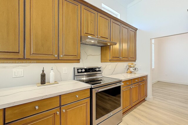 4268 SW 141st Ave, Davie, FL 33330 - kitchen with stainless steel range with electric stovetop, under cabinet range hood, light wood-style flooring, light stone counters, and brown cabinetry
