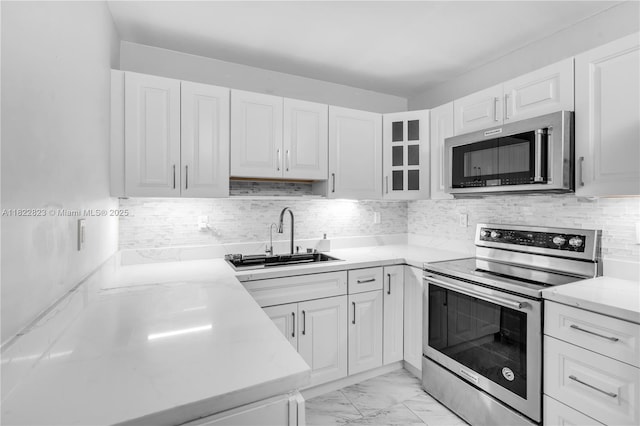 600 Three Islands Blvd Unit 310, Hallandale Beach, FL 33009 - kitchen featuring stainless steel appliances, white cabinetry, glass insert cabinets, decorative backsplash, and light marble finish flooring
